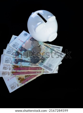 Close-up of Russian ruble with a white piggy bank on a black background.  High quality photo income and business concept.