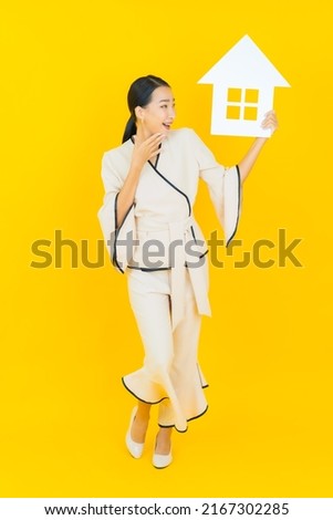 Portrait beautiful young business asian woman with home paper sign on yellow background