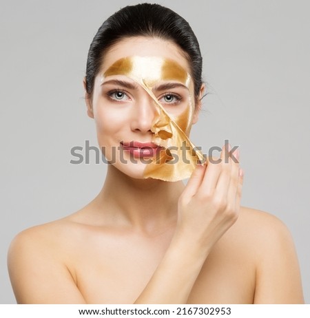 Beauty Woman peeling off Golden Facial Mask. Smooth Skin Model taking off Gold Purifying Face Film Mask over Gray. Women cleansing Cosmetics and Skincare Cosmetology Royalty-Free Stock Photo #2167302953