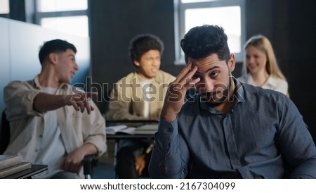 Young excited arab guy student sitting in classroom cannot concentrate on lesson being ridiculed by classmates suffering from abuse feeling distressed lonely upset concept of discrimination and racism Royalty-Free Stock Photo #2167304099