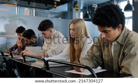 Young group of diverse serious people writing college entrance exam thinking about question difficult test students write notes essay sit in classroom at desk higher education concept at university Royalty-Free Stock Photo #2167304127