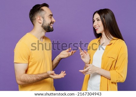 Young smiling cheerful happy cool couple two friends family man woman together in yellow casual clothes look to each other speak talk spead hands isolated on plain violet background studio portrait Royalty-Free Stock Photo #2167304943
