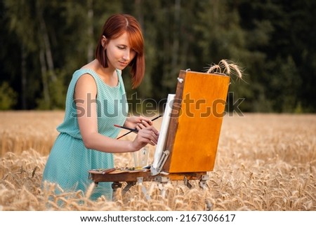 Female painter doing her job in the field of wheat. Young girl painting outdoors