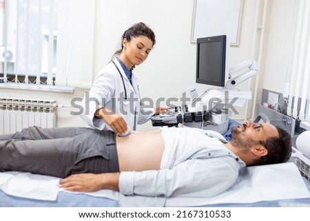Ultrasound diagnosis of the stomach on the abdominal cavity of a man in the clinic, close-up view. The doctor runs an ultrasound sensor over the patient's male abdomen. Diagnostics of internal organs. Royalty-Free Stock Photo #2167310533