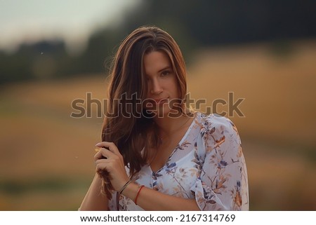 young brunette in summer with long hair in a field, happy person health beauty posing at sunset