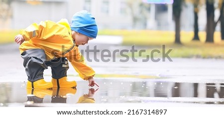boy playing outdoors in puddles, autumn childhood rubber shoes raincoat yellow Royalty-Free Stock Photo #2167314897