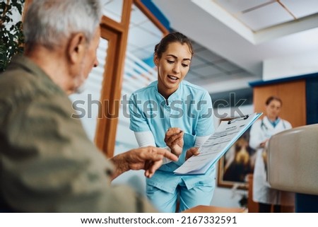 Young nurse and senior patient talking while going through his medical data at the clinic.  Royalty-Free Stock Photo #2167332591