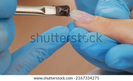 Manicurist paints nails with  gel polish. Application of acrylic polish on nails.   Application Shellac on nails.  Manicure service.  Specialist covers the nail of client by clear gel. Close up. Royalty-Free Stock Photo #2167334275