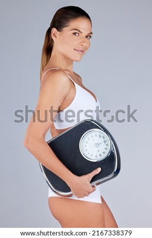 Ive shed some pounds in my weight loss journey. Studio portrait of an attractive young woman holding a scale against a grey background.
