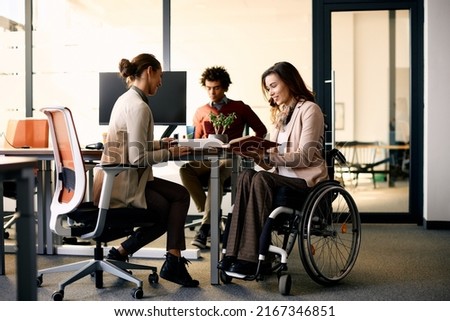 Happy businesswoman with disability and her female colleague cooperating while working on paperwork in the office.  Royalty-Free Stock Photo #2167346851