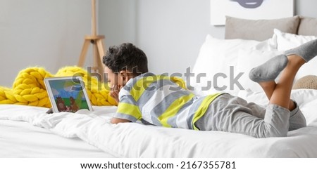 Little African-American boy with laptop watching cartoons in bedroom