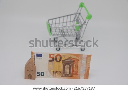 Toy house with a banknote on the background of an empty toy grocery cart, rising food prices, global food crisis