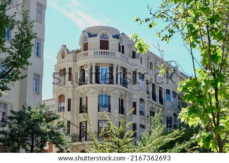Rounded corner of elegant classical facade seen through trees, Fuencarral district, center of Madrid, Spain