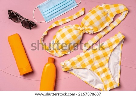 Yellow bikini with sunscreen creams and protective mask on pink background