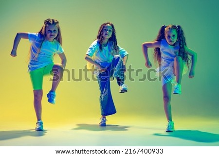 Hip-hop dance, street style. Group of children, little girls in sportive casual style clothes dancing in choreography class isolated on green background in neon light. Concept of music, fashion, art