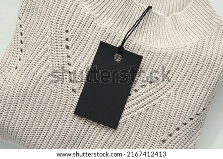  Black price tag on beige sweater, Black Friday sale concept, hang tag mockup for text, design, logo presentation.