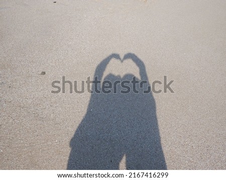 the shadows of 2 people on the beach that form like love