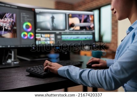 Close up shot of professional videographer sitting at desk while enhancing movie footage using specialized software. Creative company film editor expert sitting at multi monitor workstation.