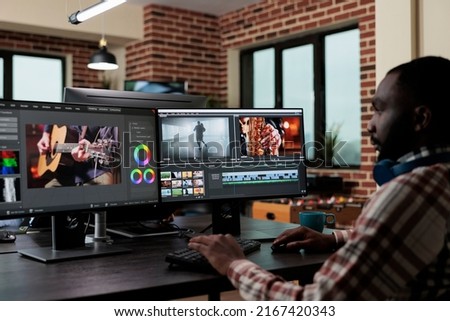 African american creative digital video editor sitting at desk while improving recorded footage visual quality. Professional post production videographer editing graphic content using specialized