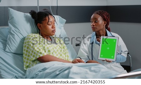 Medical specialist vertically holding green screen on tablet in hospital ward. Physician and sick person looking at gadget display with chroma key and isolated mockup background.