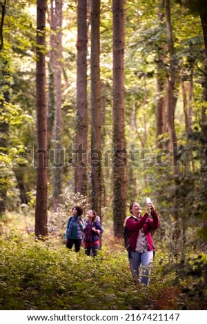 Woman Taking Photo On Mobile Phone As Group Of Female Friends On Holiday Hike Through Woods Together
