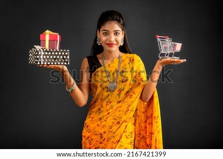 Beautiful young girl or woman holding and posing with a miniature trolley shopping cart and gift box on a gray background
