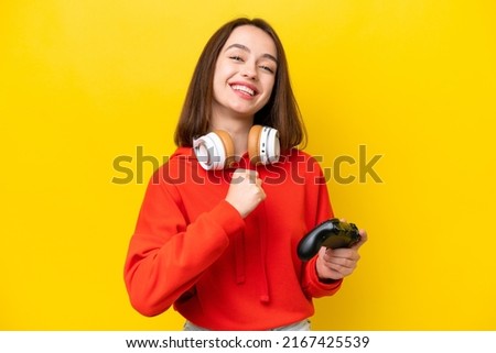 Young Ukrainian woman playing with a video game controller isolated on yellow background celebrating a victory