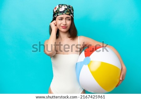 Young Ukrainian woman holding beach ball isolated on blue background frustrated and covering ears
