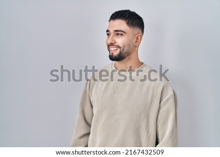 Young handsome man standing over isolated background looking away to side with smile on face, natural expression. laughing confident.  Royalty-Free Stock Photo #2167432509