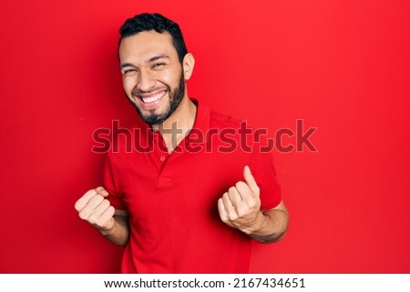 Hispanic man with beard wearing casual red t shirt very happy and excited doing winner gesture with arms raised, smiling and screaming for success. celebration concept. 