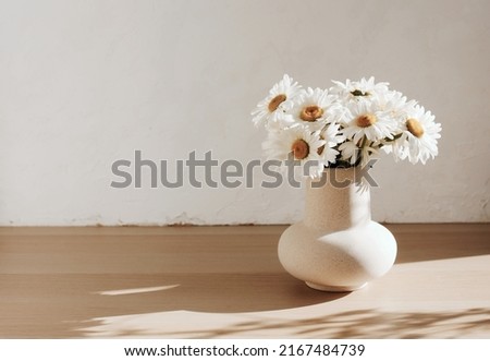 bouquet of daisies flowers in a ceramic vase on beige wooden table near a white textured wall. Copy space.Minimal Scandinavian interior. Neutral trendy colors interior decoration .