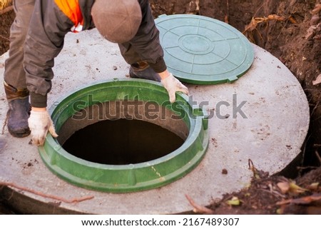 the builder installs a manhole on a concrete sewer well. Construction of a septic tank for a country house. Royalty-Free Stock Photo #2167489307