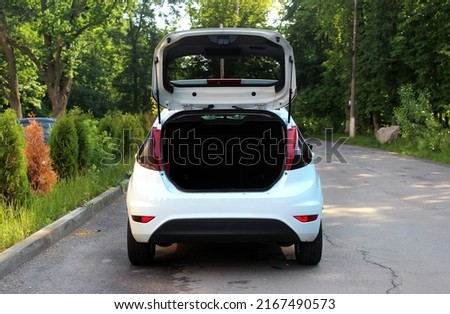 Open back door hatchback car. Clean, open empty trunk in the white car. Modern small white car with open trunk door at the city street on the background of green trees.  Royalty-Free Stock Photo #2167490573