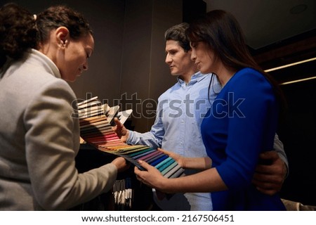Caucasian married couple holding colorful fabric samples for sofa upholstery in a furniture design store. Sales manager and interior designer demonstrates a palette of upholstery in various textures
