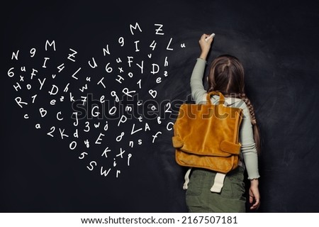 Small child girl in school uniform writing letters on a black chalkboard
