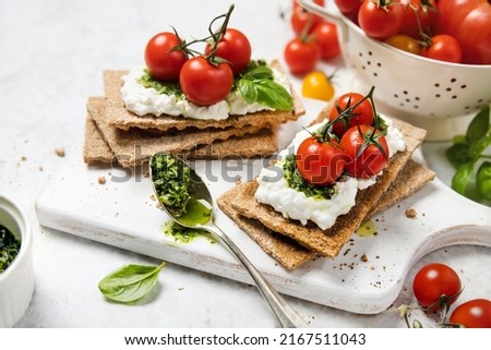 Crispbread topped with cottage cheese, whole cherry tomatoes and basil pesto, easy homemade breakfast or appetizer recipe Royalty-Free Stock Photo #2167511043