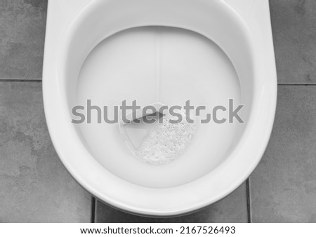 Transparent clean water with air bubbles in white toilet bowl. Focus at the center of image. Black and white image Royalty-Free Stock Photo #2167526493