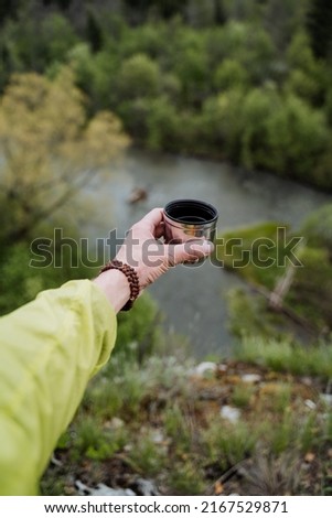 Delicious tea with taiga herbs poured into a mug, a thermal glass with a hot drink, a hand holds a cup of tea against the background of nature, a vacation in the mountains. High quality photo