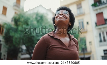 Pretty dark haired African woman standing on a street, wearing glasses. Attractive African girl looking happy exploring new city alone Royalty-Free Stock Photo #2167540605