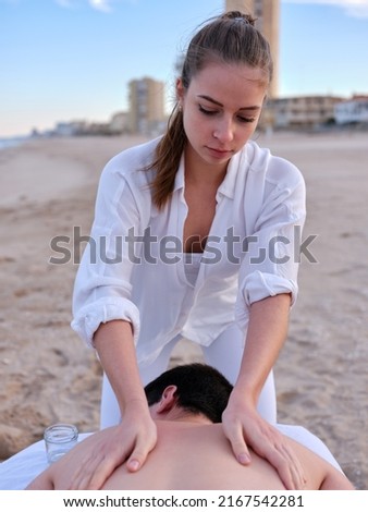 A young therapist performing a chiromassage treatment on a young man lying on a massage table outdoors on a beach in Valencia. Royalty-Free Stock Photo #2167542281