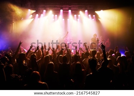 Feeling the concert vibe. Rear-view of a cheering crowd at a music concert- This concert was created for the sole purpose of this photo shoot, featuring 300 models and 3 live bands. All people in this Royalty-Free Stock Photo #2167545827