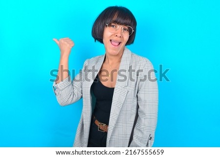 Impressed Young businesswoman with bob haircut wearing blazer against blue wall point back empty space