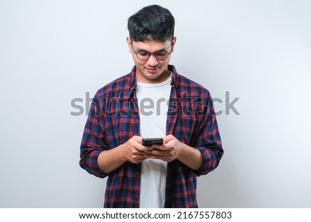 Smiling young good looking Asian man using smartphone to get in touch with family and friends isolated on white studio background