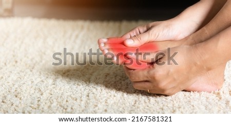 Foot pain, Asian woman holds her toe injury feeling pain her foot at home, female suffering from feet ache use hand massage relax muscle from toe in house interior, Healthcare problems medical concept Royalty-Free Stock Photo #2167581321