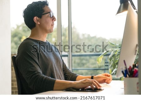 Professional working from home at his desk. Telecommuting today. Home office with minimalist design in a comfortable space. Latin man working remotely on his computer