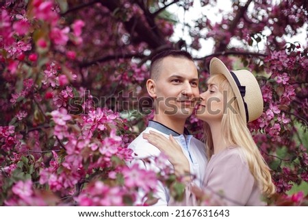 portrait man and a woman in hat stand by a blooming pink cherry tree in summer