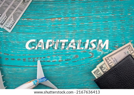 CAPITALISM - word (text) and money dollars on the table in a notepad, wallet and plane. Business concept, flight, purchase, sale, payment for services (copy space).