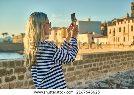 Woman traveler tourist using smartphone, taking photo of sea view at sunset in summer day. Enjoying European, Famous popular touristic place in world.