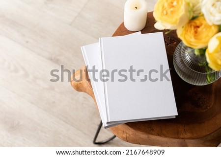 White book blank cover mockup on stylish wooden coffee table with roses bouquet, high angle view