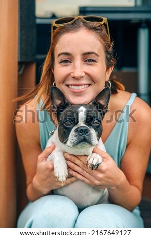 Portrait of smiling young woman hugging her boston terrier dog in front of camper van